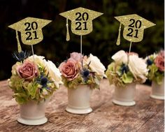 three vases with flowers and graduation hats on them are sitting on a wooden table