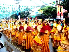 a group of women in orange and yellow dresses are marching down the street with umbrellas