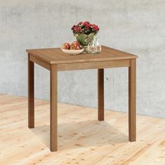 a wooden table with a bowl of fruit on it and flowers in the vase next to it