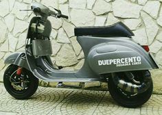 a silver scooter is parked in front of a stone wall and cobblestone