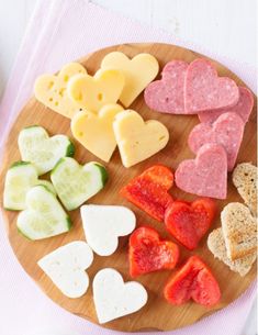 a wooden plate topped with different types of heart shaped cheeses and crackers on top of a pink towel