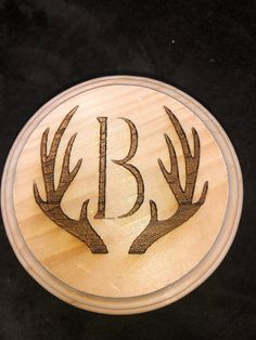 a wooden plaque with two deer antlers on it's sides and the letter b in the middle