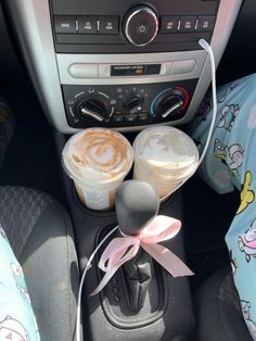 two cups of coffee sit in the center console of a car with a pink bow on it