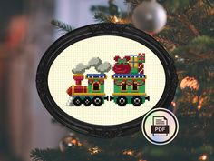 a cross stitch christmas ornament with a train on it's side hanging from a tree