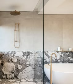 a bathtub and shower in a bathroom with marbled walls, flooring and gold fixtures