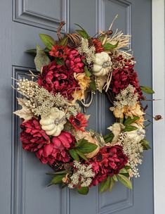 a wreath on the front door with flowers and leaves hanging from it's side