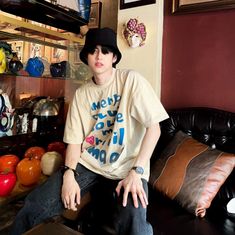 a young man sitting on top of a black leather couch in front of a shelf filled with vases