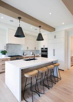 a kitchen with three stools next to an island and two lights hanging from the ceiling