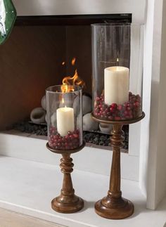 two candles are sitting in front of a fire place with berries on the top and bottom