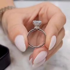 a woman's hand holding a ring with a diamond on it and white nails