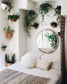 a white bed topped with lots of plants next to a mirror and potted plants