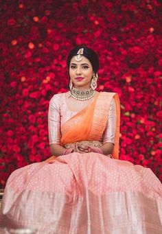 a woman sitting on top of a wooden bench wearing a pink and orange lehenga