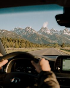 a person driving a car down a road with mountains in the background