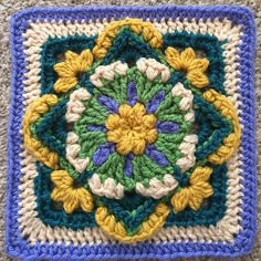 a crocheted square with yellow and blue flowers in the center, on carpet