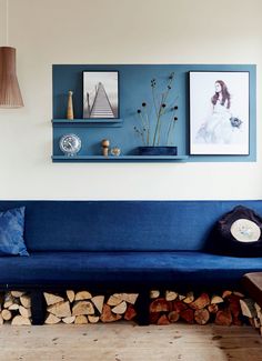 a blue couch sitting next to a pile of firewood in a living room on top of a hard wood floor