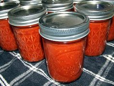 several jars with lids are lined up on a table cloth, one is empty and the other has no lid