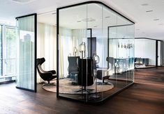 an office with glass walls and chairs in the center, surrounded by wood flooring