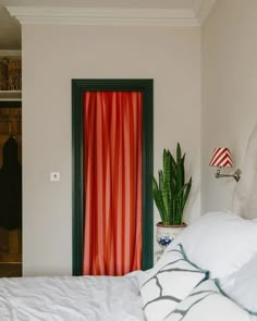 a bed with white sheets and pillows in front of a red curtained closet door