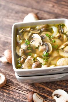 a white bowl filled with mushroom soup on top of a wooden table next to mushrooms