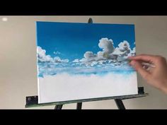 someone is painting clouds in the sky on an easel