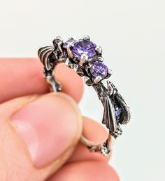 a close up of a person's hand holding an ornate ring with purple stones