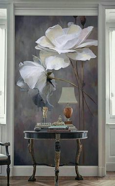 a painting of white flowers on a gray wall next to a table with a lamp