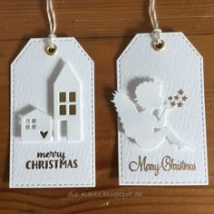 two tags with christmas images on them hanging from strings, one has a house and the other is a cupid