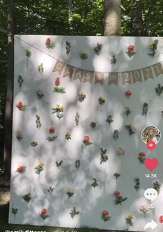 a sign with flowers on it in the woods next to a tree and two people's faces