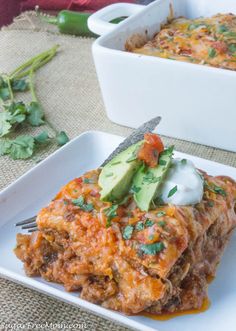 a white plate topped with lasagna covered in cheese and avocado next to a casserole dish