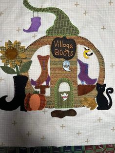 a quilted wall hanging with an image of a house and two cats on it