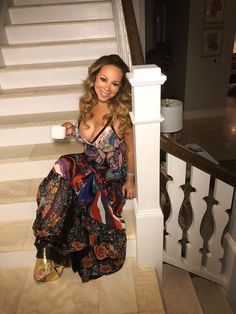 a woman is sitting on the stairs with a cup in her hand and looking at the camera