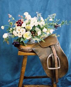 a saddle with flowers in it sitting on a wooden stool next to a blue background