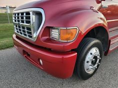 the front end of a red truck parked in a parking lot next to a grass field