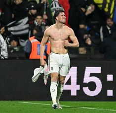 a shirtless soccer player walks on the field with his hand in his pocket as fans look on