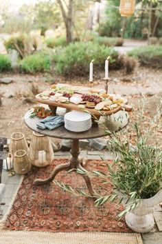 a table with food on it in the middle of an outdoor area, surrounded by greenery and candles