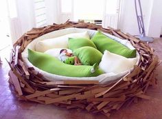 there is a bird nest with two green birds in it and pillows on the bottom