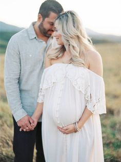 a pregnant couple standing in a field holding hands