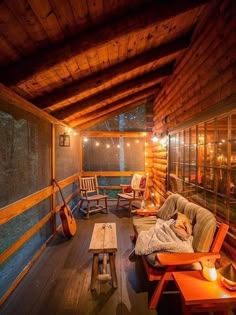 a porch with wooden furniture and string lights on the ceiling is lit up at night