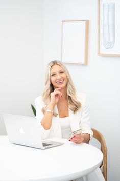 a woman sitting at a table with a laptop in front of her, smiling for the camera