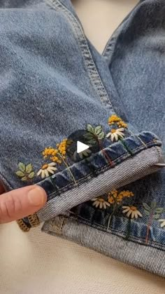 someone is holding their hand in the pocket of some jean pants with flowers on them