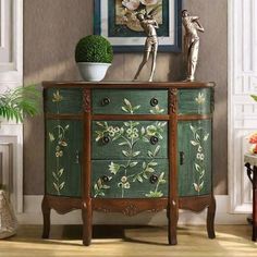 a green painted dresser with flowers on the top and two figures standing on it's sides