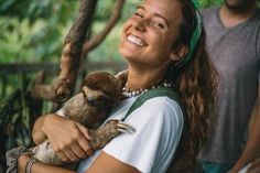 a woman holding a baby sloth in her arms