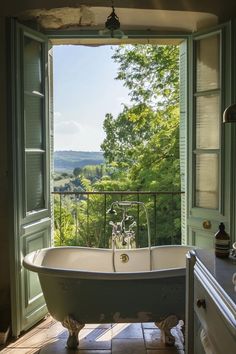 an old fashioned bathtub sits in front of a window overlooking the trees and hills