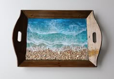 a wooden tray with an ocean scene painted on the front and sides, along with shells in the bottom