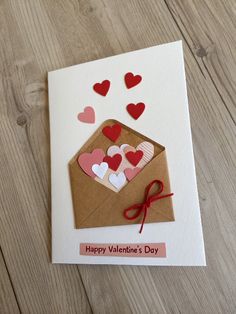 a valentine's day card with hearts coming out of an envelope on a wooden table