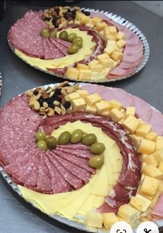 two plates with meat, cheese and olives on them sitting on a counter top