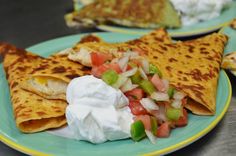 three quesadillas with sour cream and vegetables on a blue plate next to other food items