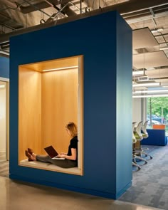 a woman sitting in a blue cubicle reading a book