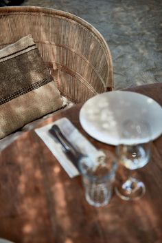 the table is set with two empty glasses and a plate on it, next to a brown wicker chair