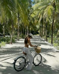 a woman riding a bike down a dirt road next to palm tree lined forest filled with lots of trees